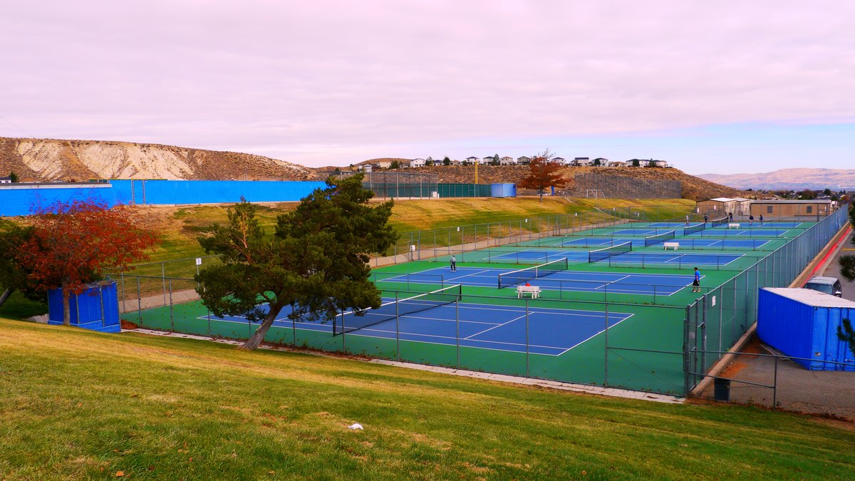 Empty outdoor high school tennis courts with green and blue surfaces surrounded by fencing